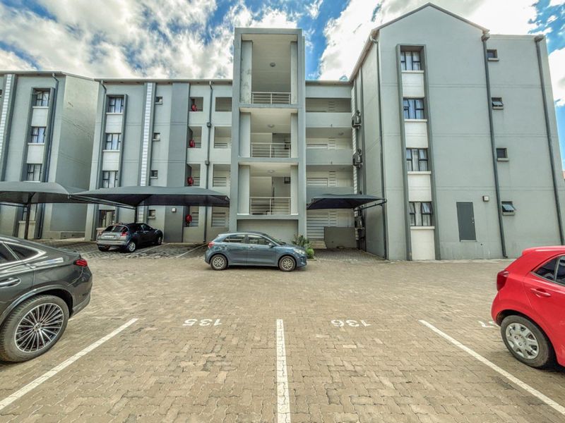 Exterior view of a modern apartment complex featuring paved parking bays, covered carports, and multi-level residential units with balconies.