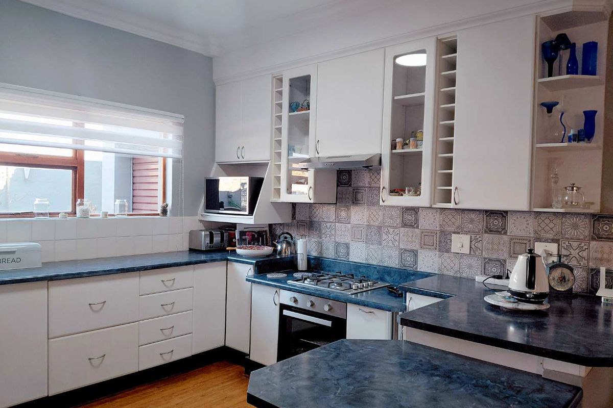 A functional kitchen featuring white cabinetry, dark laminate countertops, a gas hob, built-in oven, and decorative tiled backsplash with timber flooring.