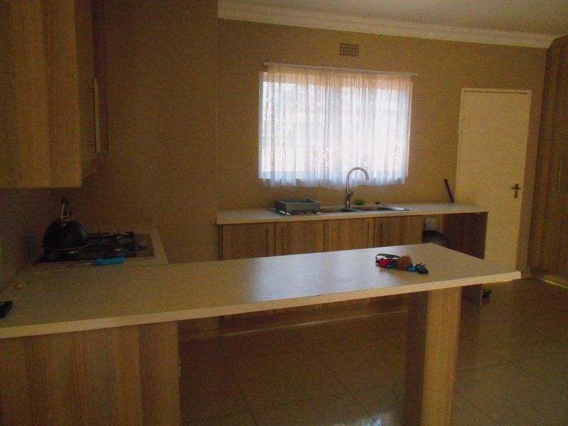 A functional kitchen featuring light wood-look cabinetry, laminate countertops, a built-in hob, and tiled flooring with a window providing natural light.