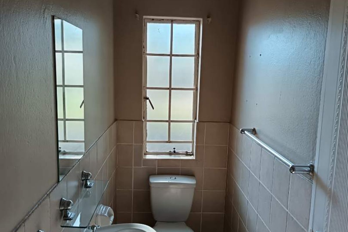 A compact bathroom featuring a pedestal basin, toilet, tiled walls, and a window, providing functional utility in a neutral, dated finish.