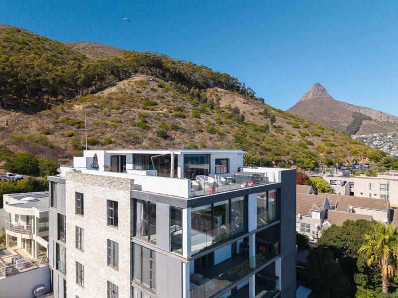 Aerial view of a modern penthouse apartment building featuring extensive glass facades, a rooftop terrace, and stone exterior finishes against a mountain backdrop.