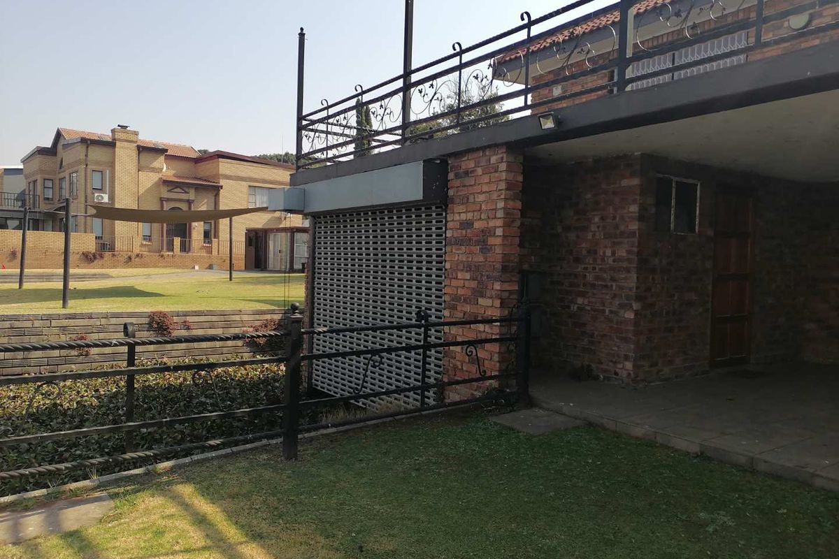 Rear exterior view featuring a brick facade, a security roller shutter, and an elevated balcony with wrought iron railings overlooking the garden.