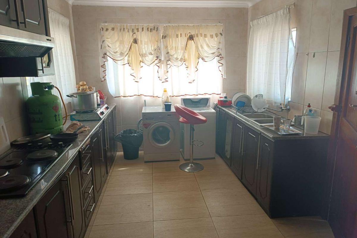 A functional kitchen featuring dark wood cabinetry, granite countertops, tiled walls, and integrated laundry appliances.