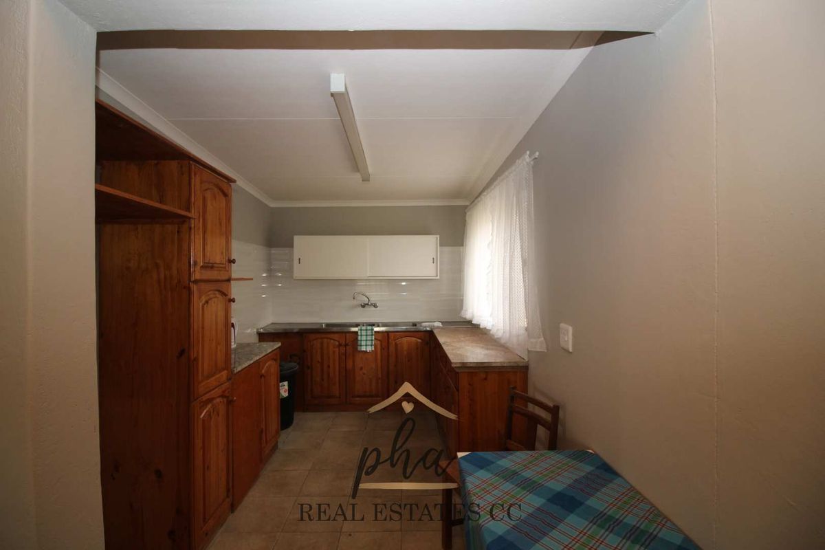 A functional kitchen featuring wooden cabinetry, tiled flooring, and a stainless steel sink, offering a practical layout for daily meal preparation.