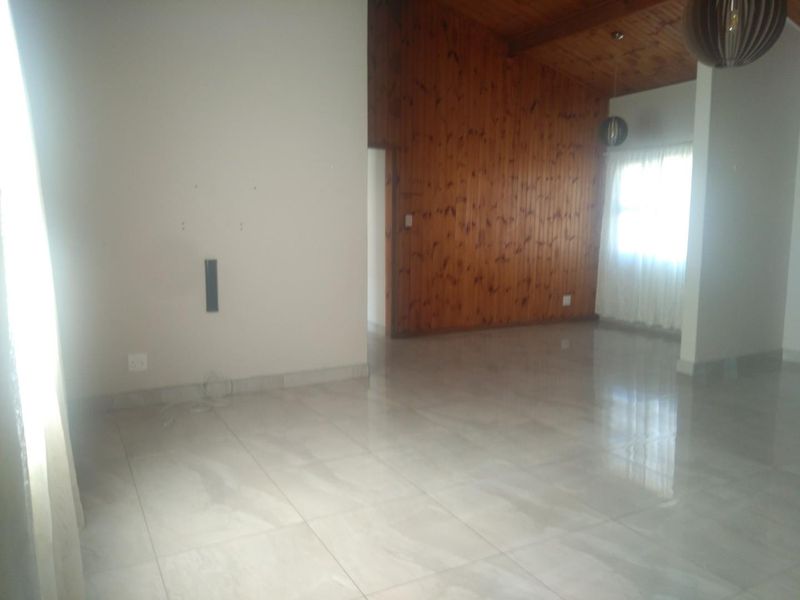 An empty living room featuring polished tiled floors and a vaulted timber-paneled ceiling with natural light.