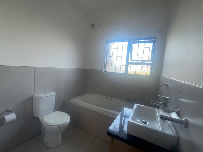 A clean, functional bathroom featuring a bathtub, toilet, and a vanity basin with a granite countertop, finished with neutral wall and floor tiles.