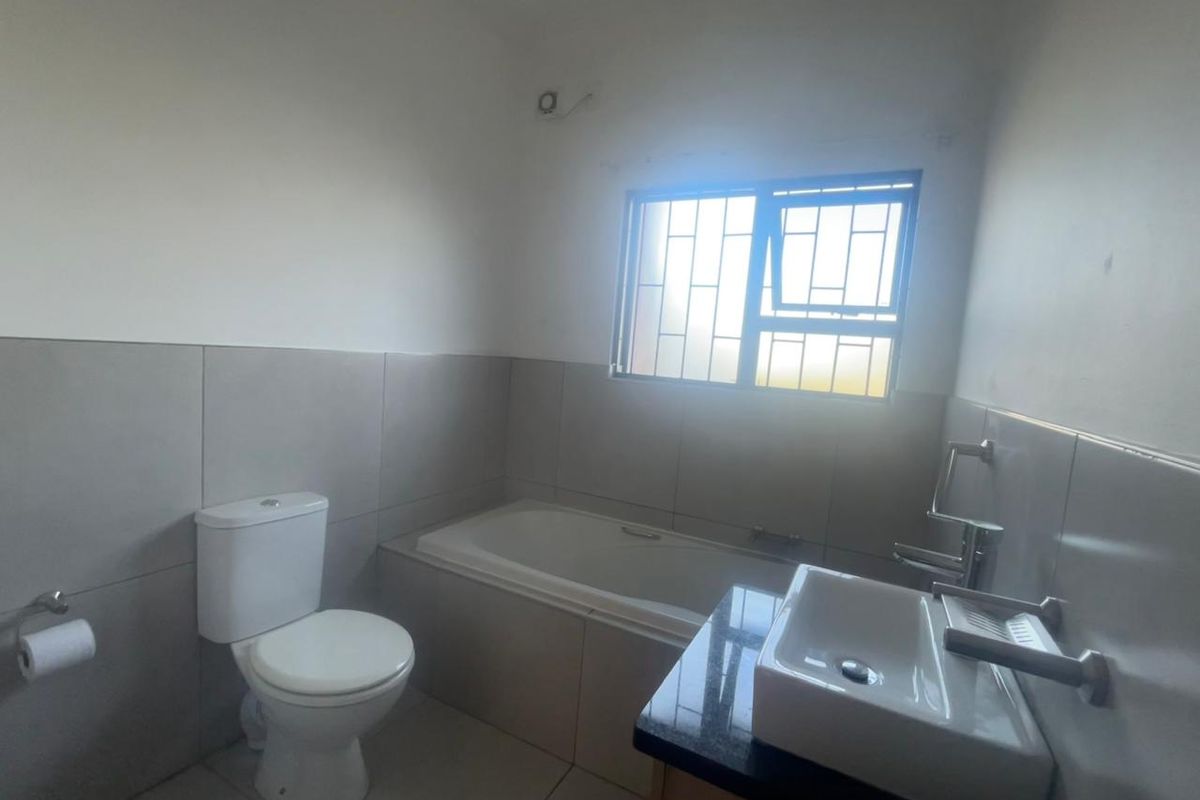 A clean, functional bathroom featuring a bathtub, toilet, and a vanity basin with a granite countertop, finished with neutral wall and floor tiles.