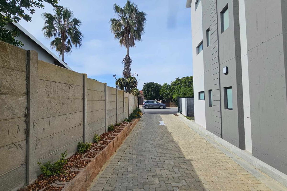 A paved driveway leading to the street, featuring a precast concrete boundary wall and modern apartment building exterior.