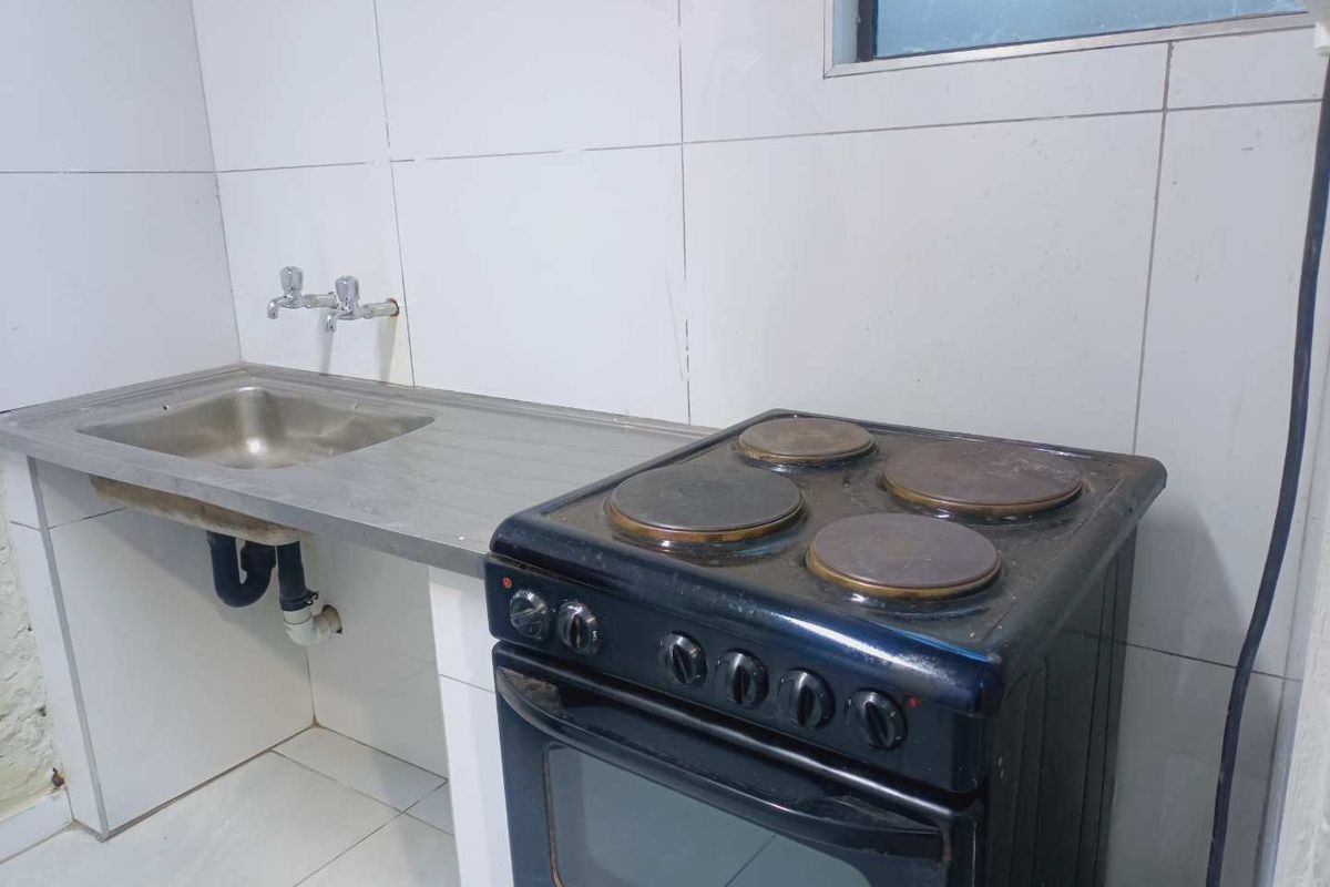 A compact kitchen area featuring a stainless steel sink, tiled walls, and a freestanding electric stove.