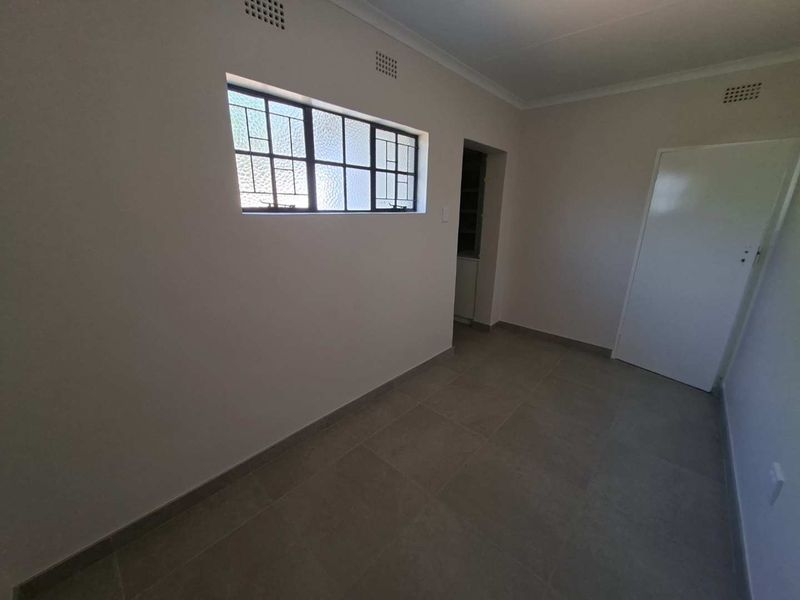 A clean, empty bedroom featuring neutral tiled flooring, a steel-framed window, and a simple interior door, ready for personalization.
