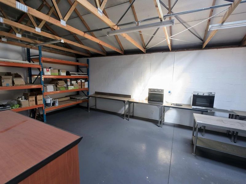 Industrial utility space featuring exposed timber roof trusses, painted block walls, durable epoxy flooring, and integrated oven units for functional workspace use.