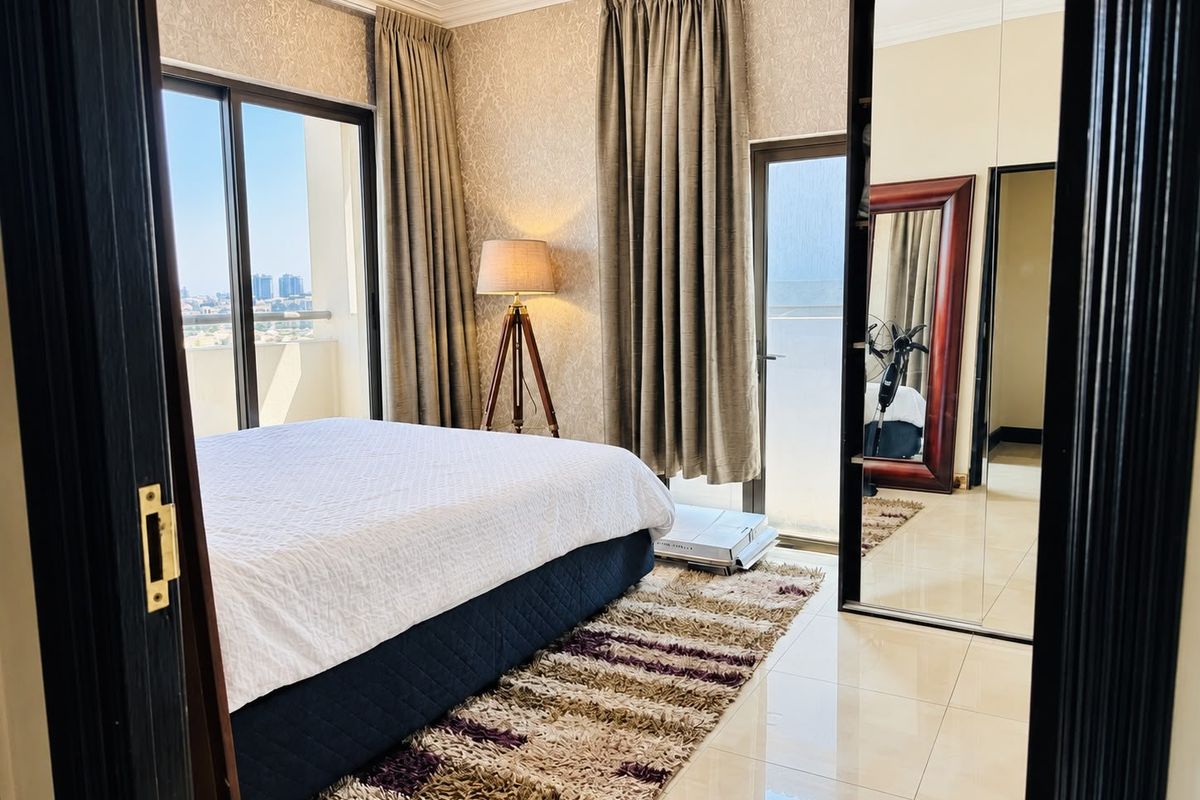 A well-lit bedroom featuring tiled flooring, built-in mirrored wardrobes, and sliding glass doors providing access to an outdoor balcony area.