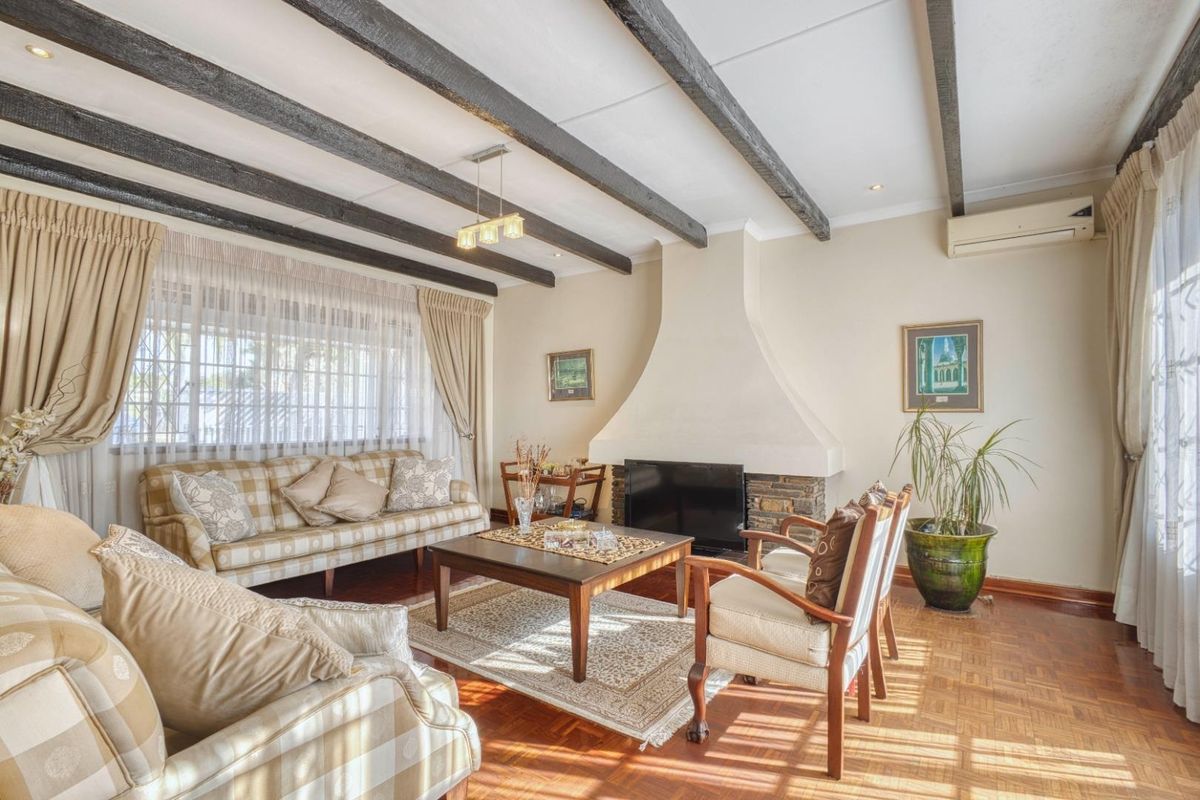 A cozy living room featuring exposed timber ceiling beams, a prominent built-in fireplace, and classic parquet flooring, creating a warm and inviting atmosphere.