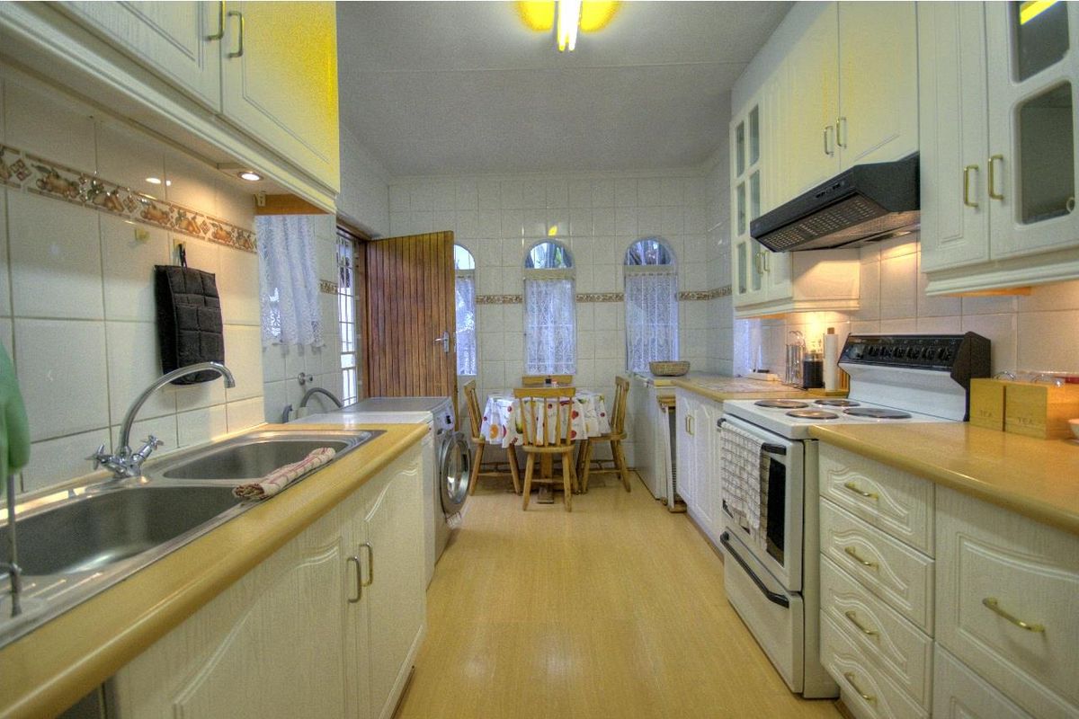A functional kitchen featuring white cabinetry, laminate countertops, tiled splashbacks, and an integrated stove with extractor fan, with an adjacent dining area.