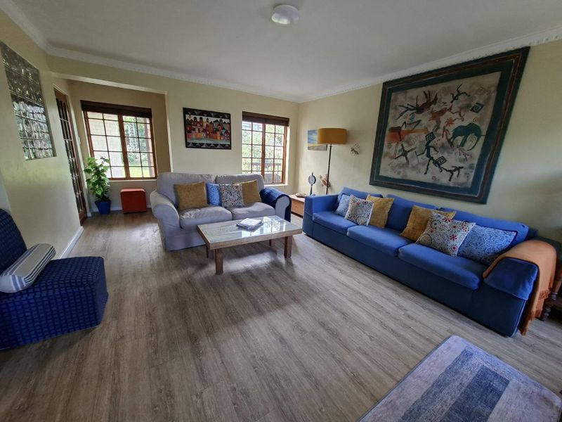 A spacious living room featuring laminate flooring, timber-framed windows, and a unique glass block feature wall, offering a comfortable and well-lit living space.