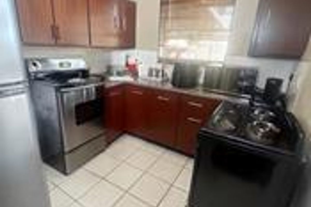 A functional kitchen featuring wooden cabinetry, tiled flooring, and a stainless steel stove, offering a practical layout for daily meal preparation.