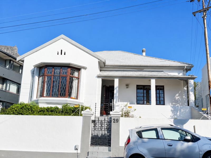 Front elevation of a charming single-story house featuring a bay window, covered porch, and secure perimeter wall with a wrought iron gate.