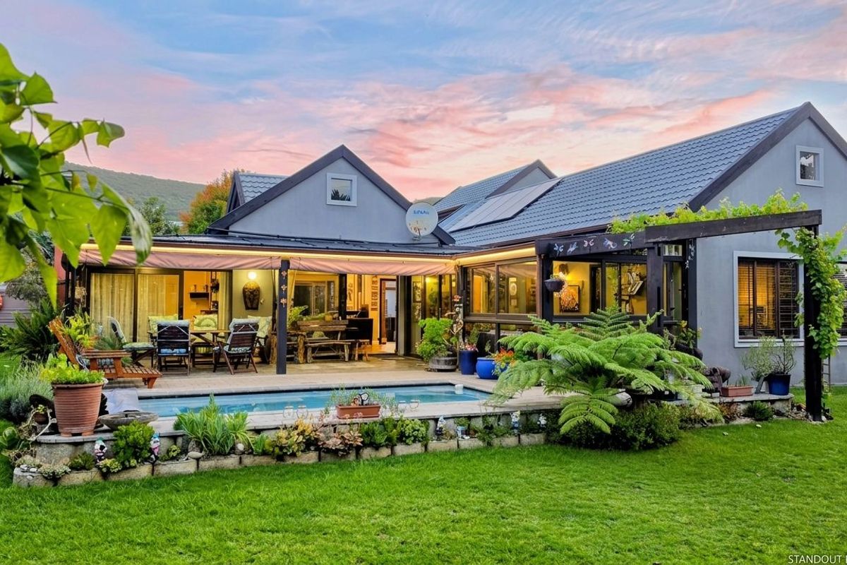 A well-maintained rear exterior featuring a swimming pool, timber decking, and a pergola, set against a landscaped garden with mountain views.