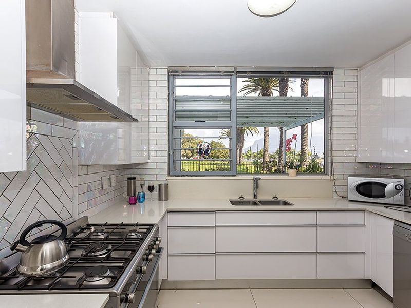 Modern kitchen featuring white cabinetry, stone countertops, subway tile backsplash, gas stove with extractor, and a double basin sink overlooking the garden.