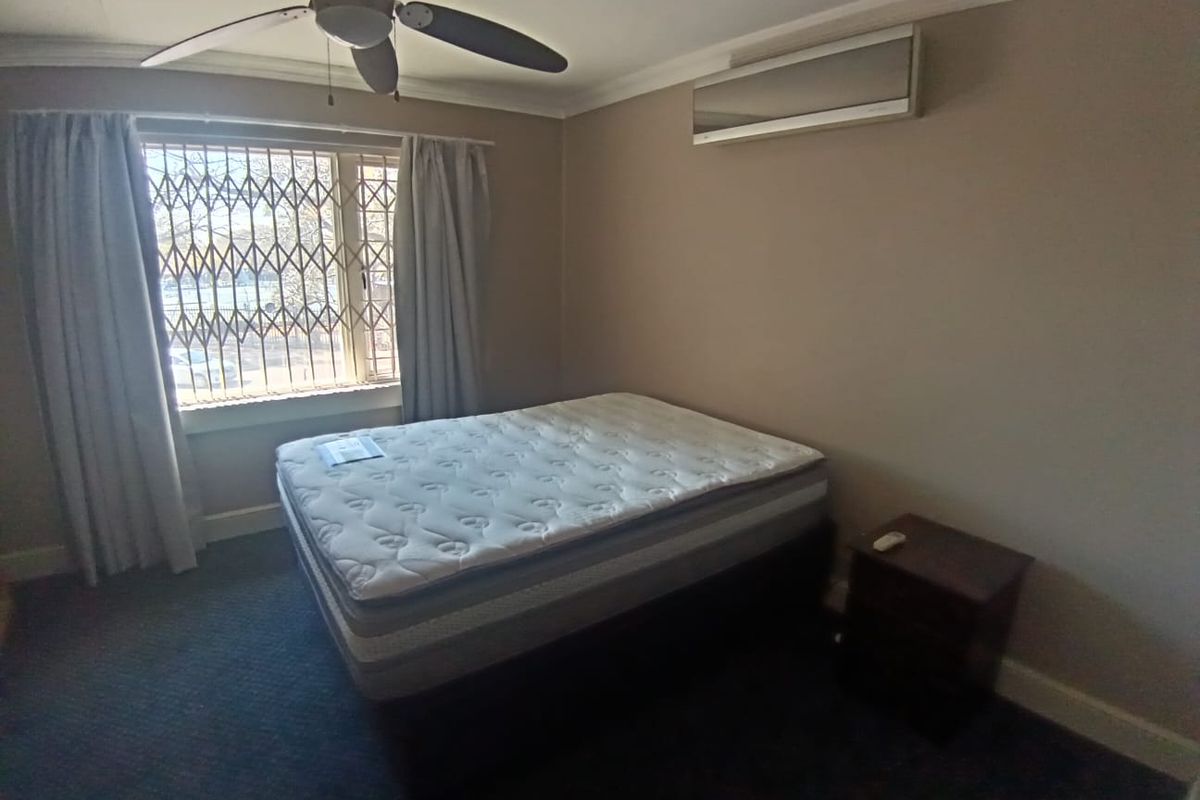 A bedroom featuring a ceiling fan, wall-mounted air conditioning unit, and security bars on the window.
