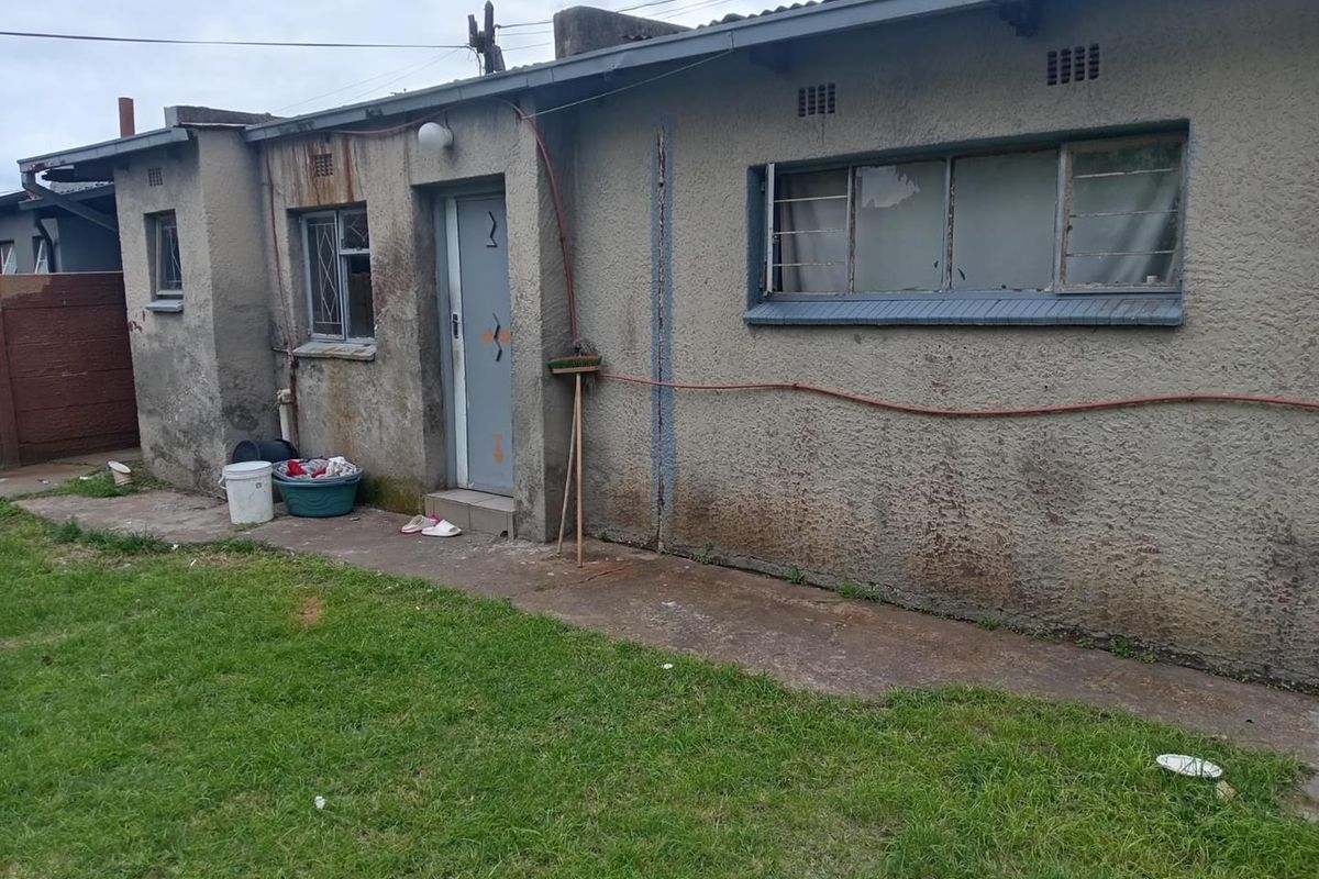 Rear exterior view of the property showing a concrete pathway, grass area, and the building facade with visible wear and maintenance requirements.