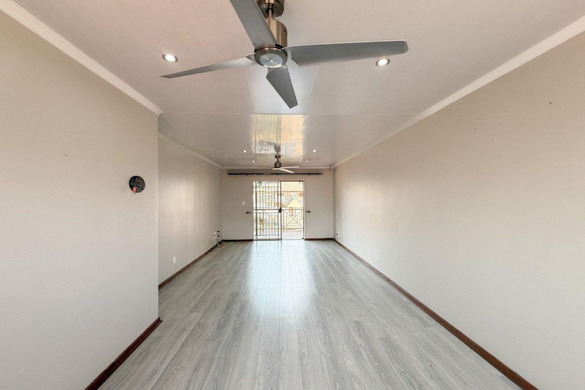A spacious, empty living area featuring light-toned laminate flooring, recessed ceiling lighting, and a modern ceiling fan, leading to a secure balcony entrance.