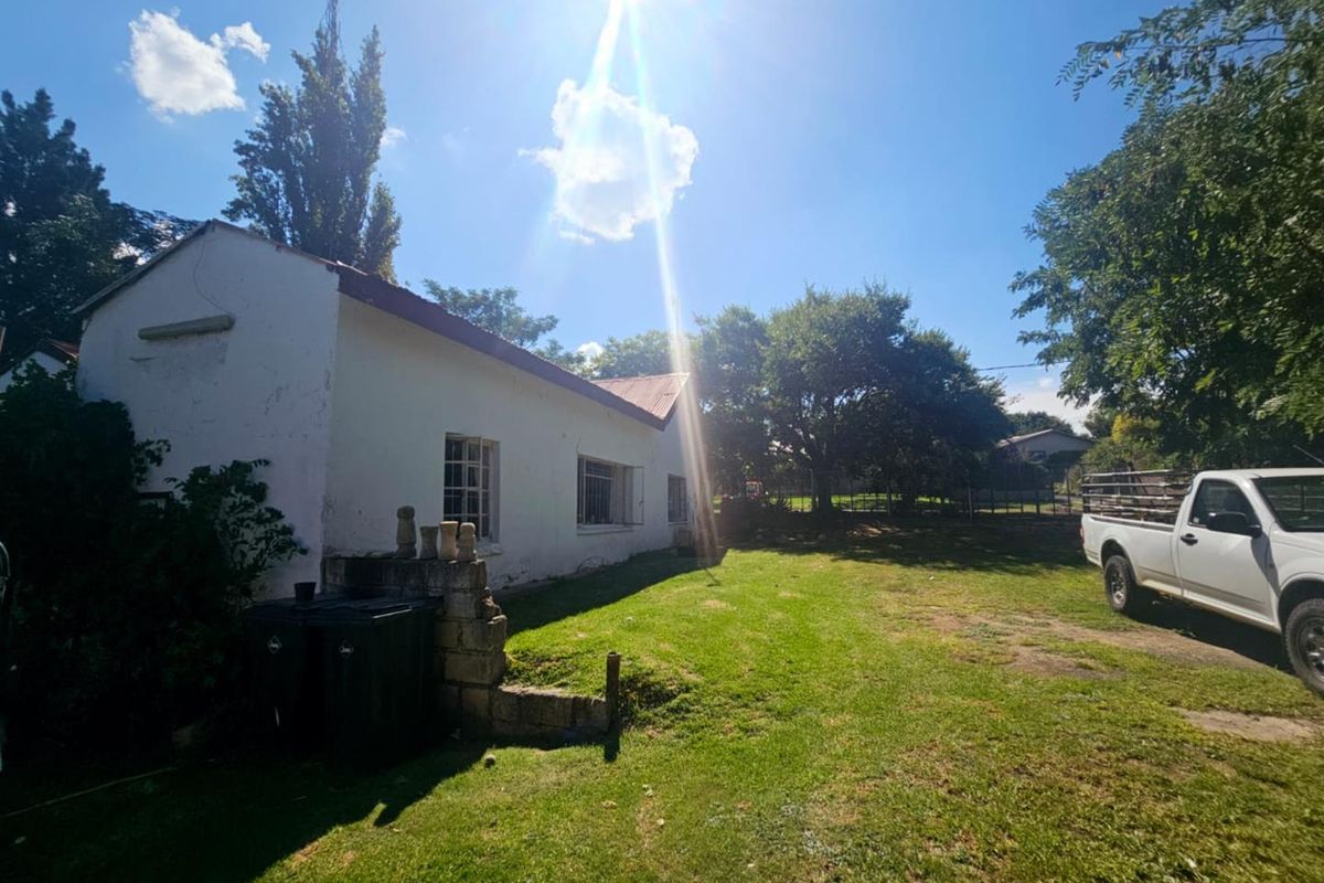 Rear view of the property showing the exterior wall, lawn area, and surrounding garden space.