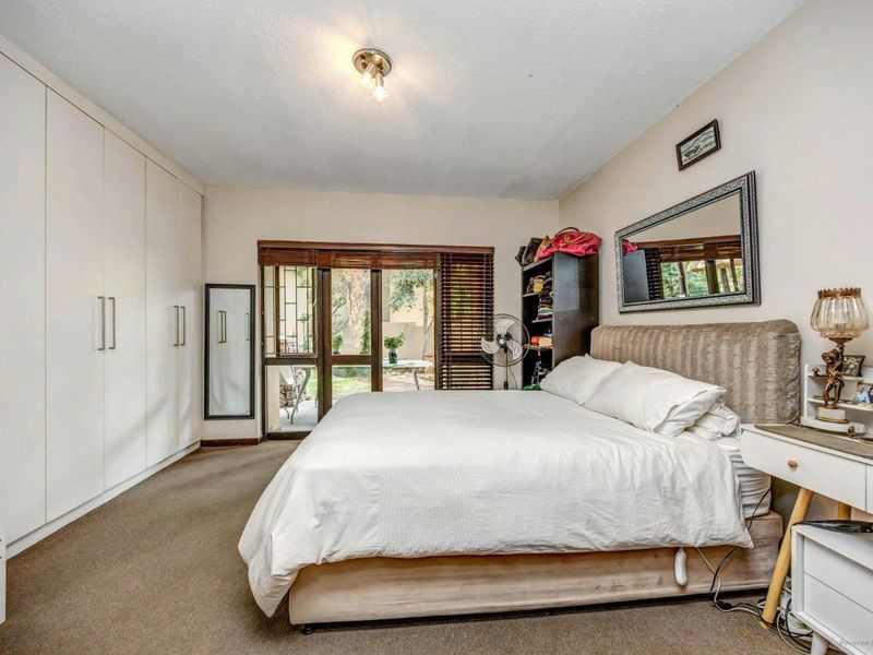 Spacious bedroom featuring extensive built-in cupboards, carpeted flooring, and a sliding glass door providing direct access to the garden area.