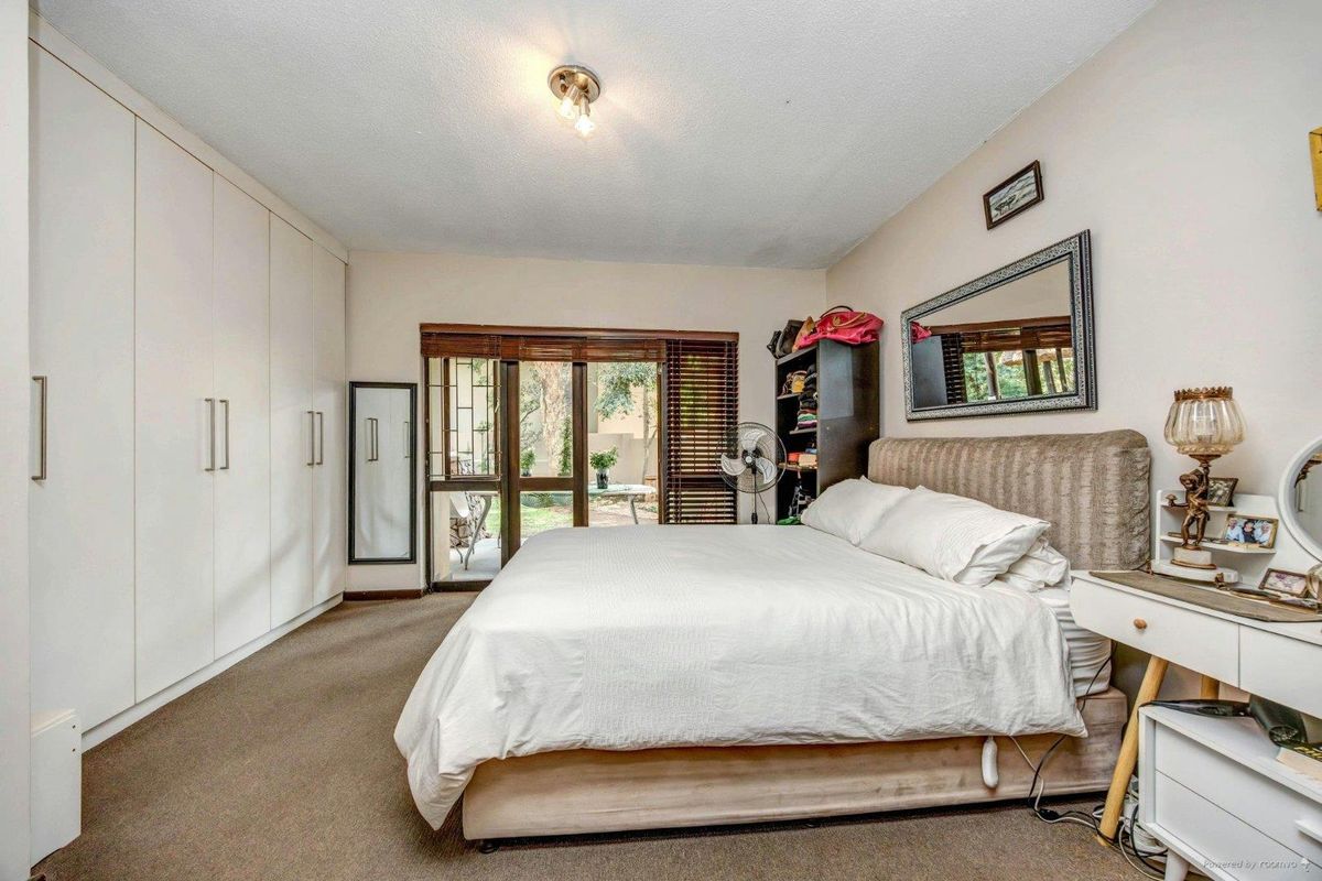 Spacious bedroom featuring extensive built-in cupboards, carpeted flooring, and a sliding glass door providing direct access to the garden area.