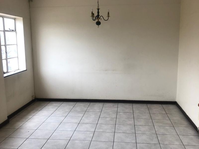 An empty living room featuring tiled flooring, a multi-pane window, and a central ceiling light fixture, ready for renovation or staging.