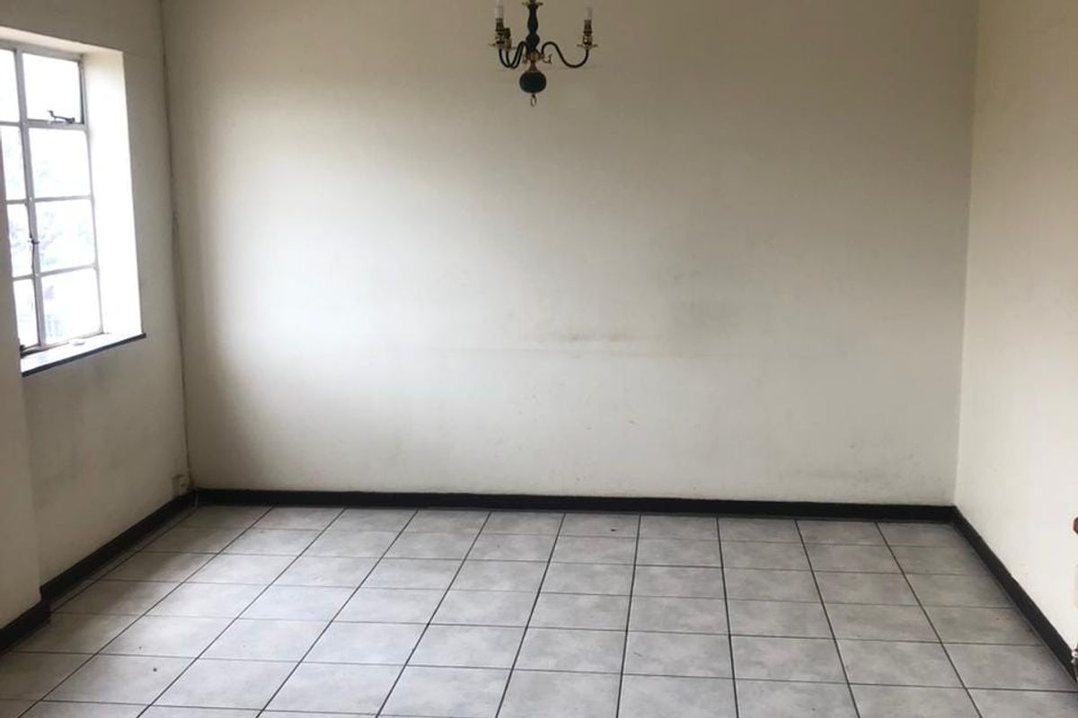 An empty living room featuring tiled flooring, a multi-pane window, and a central ceiling light fixture, ready for renovation or staging.