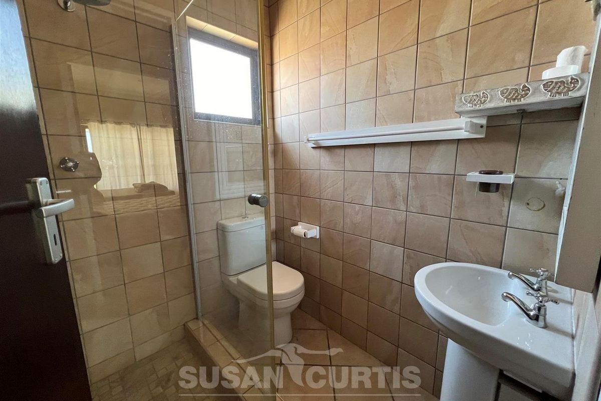 A compact bathroom featuring a glass-enclosed shower, pedestal basin, and toilet with neutral wall tiling.