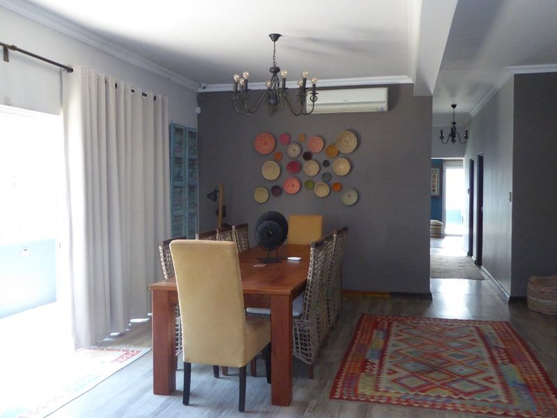 A well-lit dining room featuring laminate flooring, cove cornicing, and a wall-mounted split-system air conditioner, providing a comfortable space for family meals.