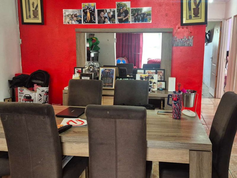 A dining room featuring tiled flooring, red accent wall, and built-in mirror, adjacent to a kitchen area.