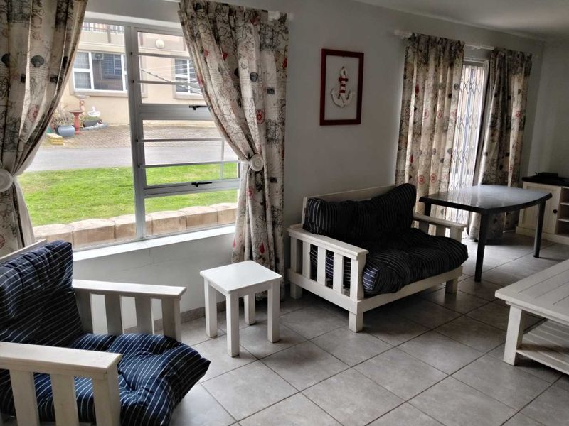 A bright living area featuring tiled flooring, large windows with security bars, and direct access to the exterior through a security gate.