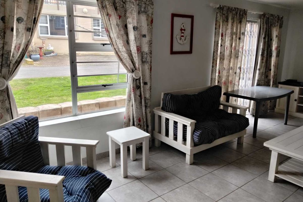 A bright living area featuring tiled flooring, large windows with security bars, and direct access to the exterior through a security gate.