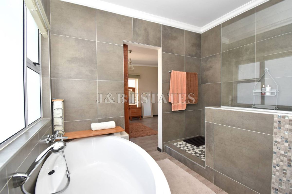 Modern bathroom featuring large format grey wall tiles, a freestanding bathtub, and a walk-in shower with a glass partition.