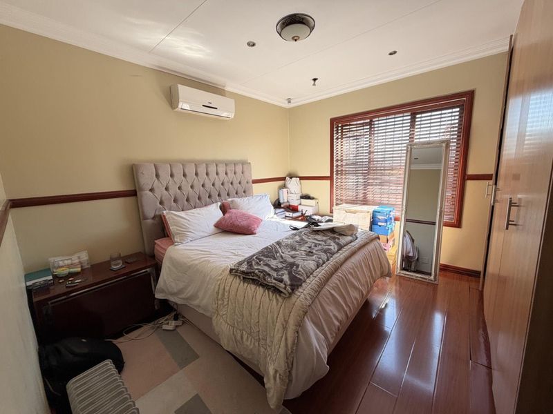 A bedroom featuring laminate flooring, built-in cupboards, an air conditioning unit, and wooden venetian blinds.