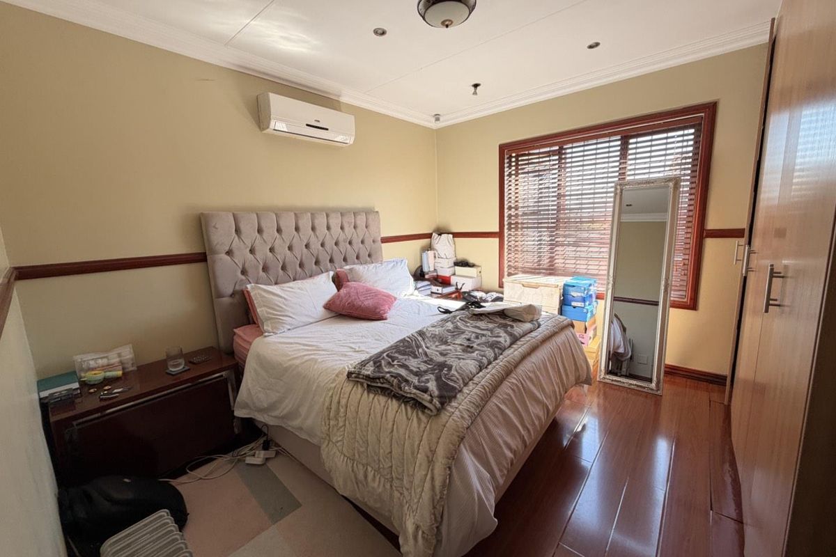 A bedroom featuring laminate flooring, built-in cupboards, an air conditioning unit, and wooden venetian blinds.