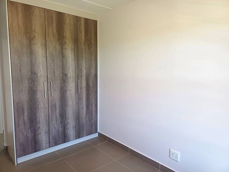 A clean, empty bedroom featuring modern wood-finish built-in wardrobes and neutral tiled flooring, providing a versatile space ready for personalization.