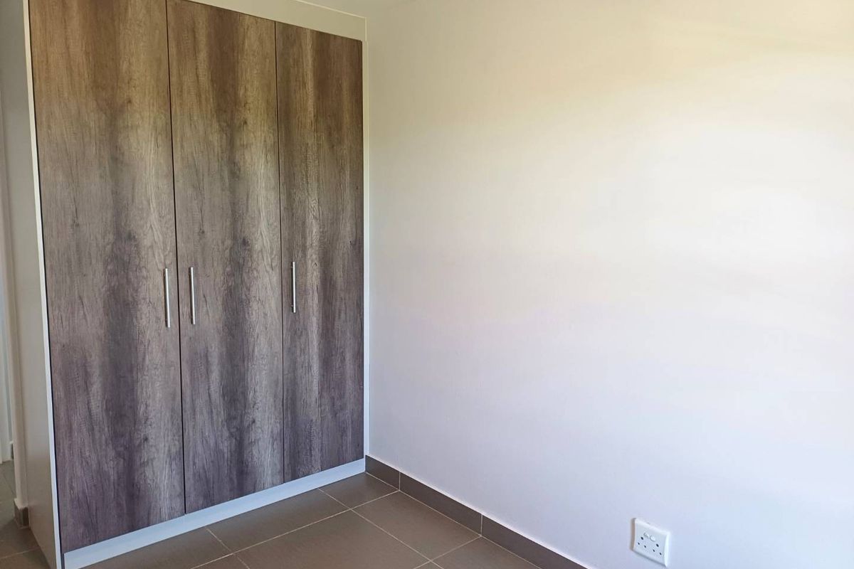 A clean, empty bedroom featuring modern wood-finish built-in wardrobes and neutral tiled flooring, providing a versatile space ready for personalization.