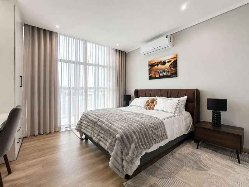 A well-maintained bedroom featuring laminate flooring, built-in cabinetry, an air conditioning unit, and large windows with floor-to-ceiling curtains.