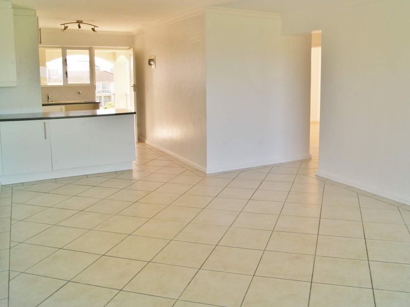 An open-plan living and kitchen area featuring neutral tiled flooring, white cabinetry, and direct access to an outdoor balcony space.