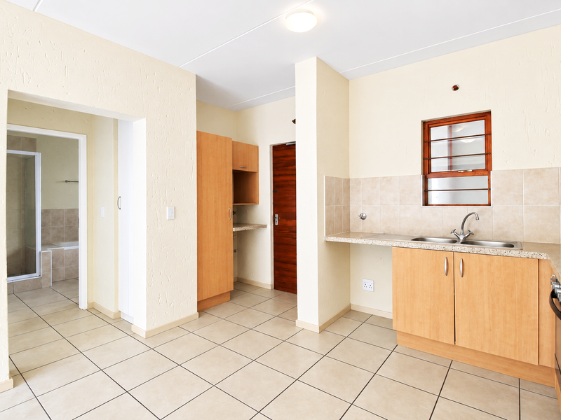 A functional kitchen featuring built-in cabinetry, a double sink, tiled backsplash, and integrated oven and hob, with an adjacent view into the bathroom.