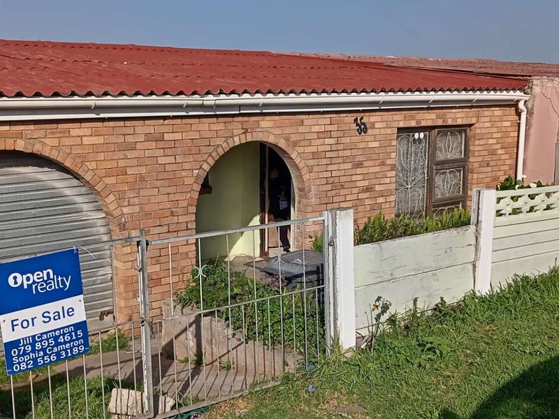 Front exterior view of a face brick house featuring a corrugated roof, arched entrance, and a roller shutter garage door with a boundary wall.