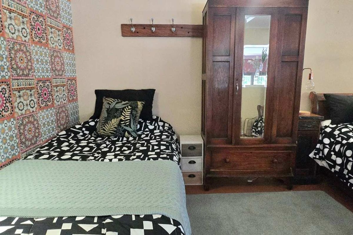 A bedroom featuring patterned wallpaper, wooden wardrobe, and space for multiple beds.