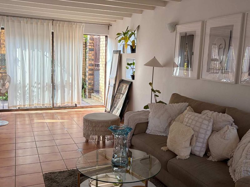 A bright living room featuring terracotta floor tiles, exposed beam ceilings, and sliding glass doors that provide access to an outdoor patio area.