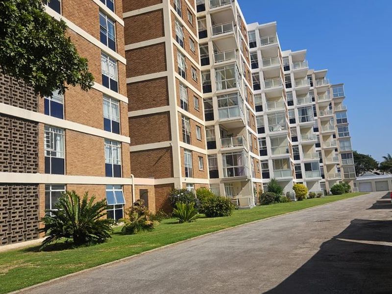 Exterior view of a multi-story apartment complex featuring brick facade, private balconies, and a paved driveway with surrounding landscaped lawn.