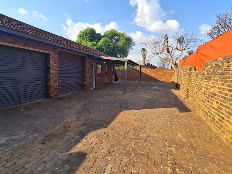 A spacious exterior view featuring a double garage with roller doors, paved driveway, and enclosed perimeter brick walling.