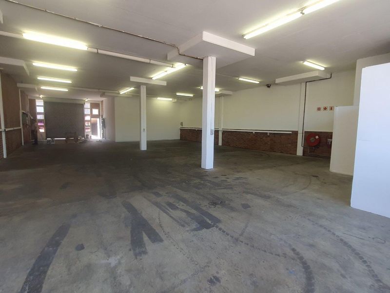 Spacious open-plan industrial unit featuring concrete flooring, exposed brick accents, structural columns, and functional fluorescent lighting throughout the expansive workspace.